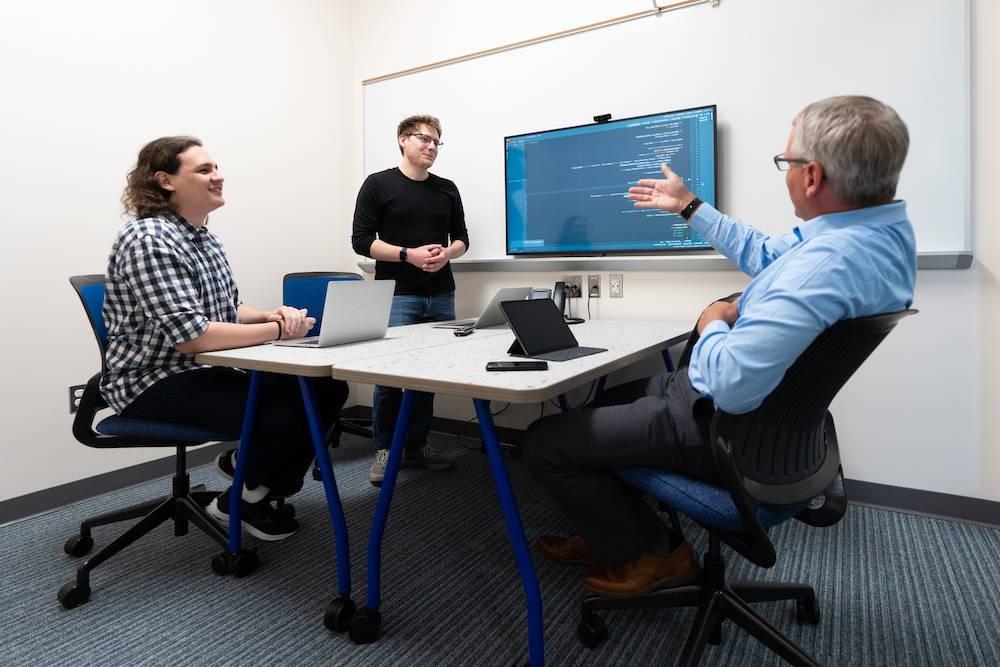 Students sitting at a table looking at a television with a professor